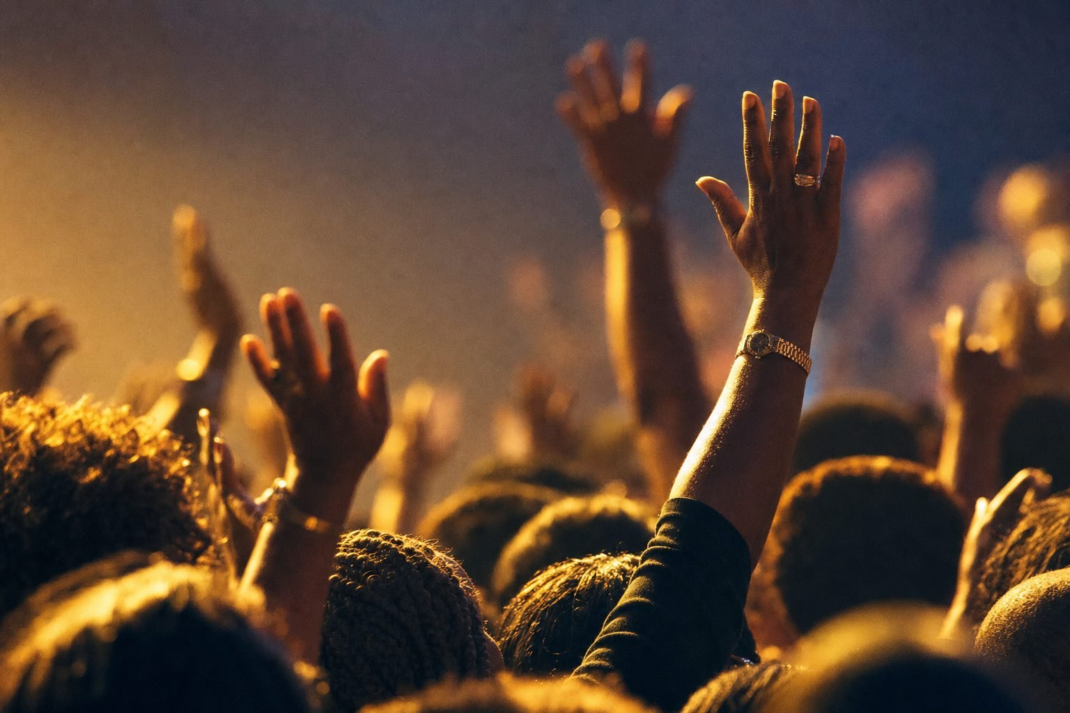 Worshippers with hands raised at a live gospel performance, lit in warm gold light