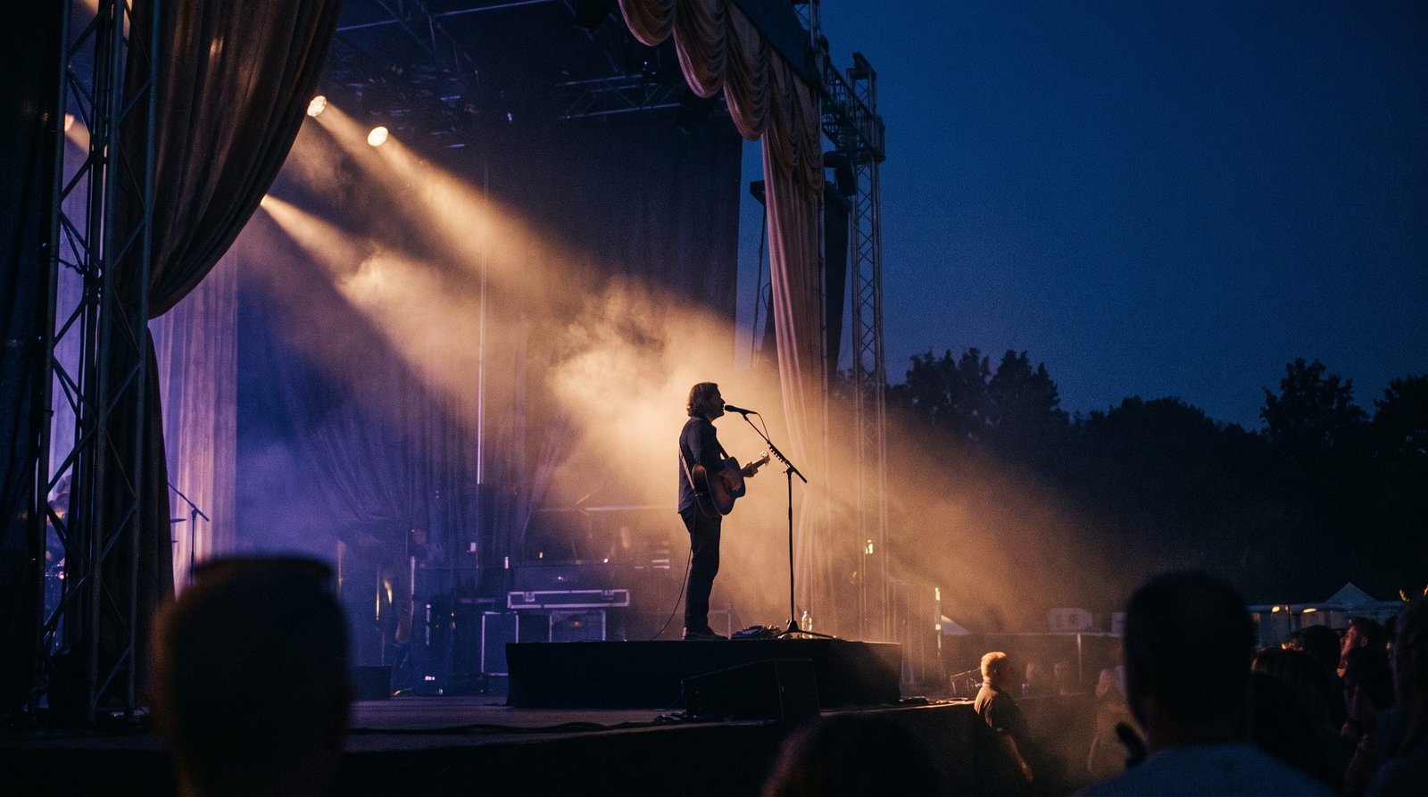 A worship artist performing on stage under golden spotlight beams